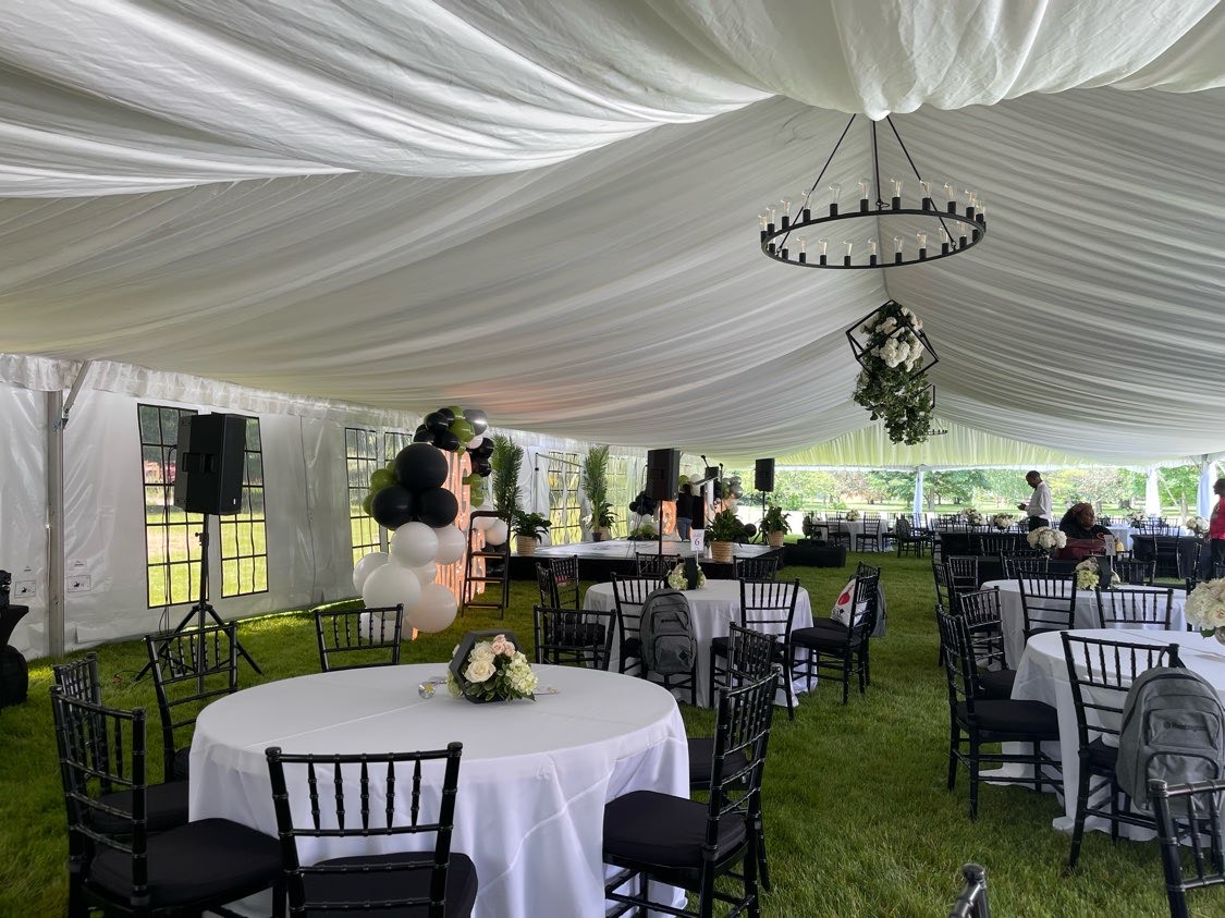 Elegant wedding reception tent with black chiavari chairs, round tables, chandelier, and tent liner